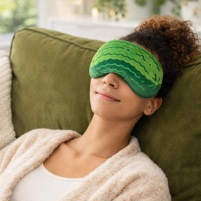 Person wearing a pickle shaped sleep mask, sitting on a green couch.