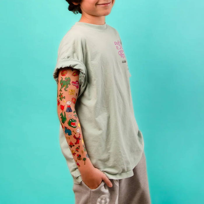 Child wearing a light gray t-shirt with colorful dinosaur-themed arm tattoos against a teal background.