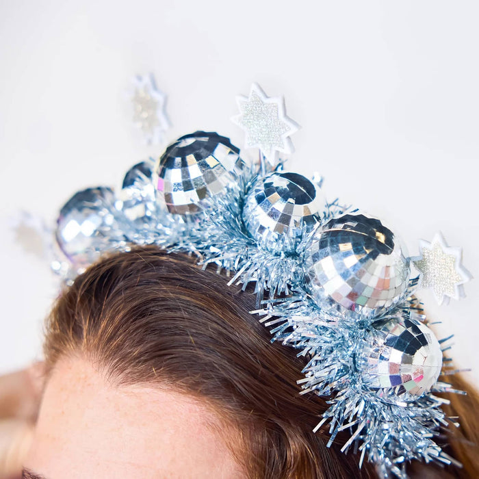 A close-up of a person wearing a festive silver tinsel headband decorated with disco ball ornaments and white and silver felt star accents.