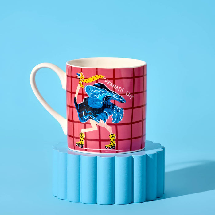 A white ceramic mug featuring a pink and red grid pattern with an illustration of an ostrich with yellow leopard-print boot roller skates with the text 'DRAMATIC EXIT', handle is on the left and it's displayed on a blue fluted pedestal against a solid blue background.