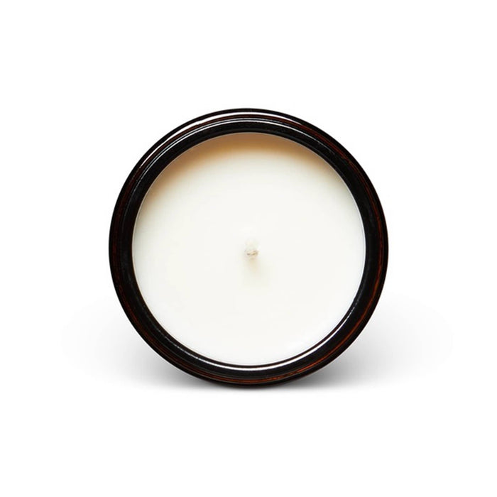 A top-down view of a round, three-wick candle with creamy off-white wax and a dark amber rim, set against a plain white background.