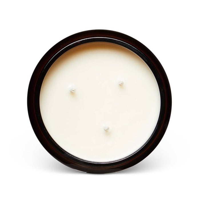 A top-down view of a round, three-wick candle with creamy off-white wax and a dark amber rim, set against a plain white background.