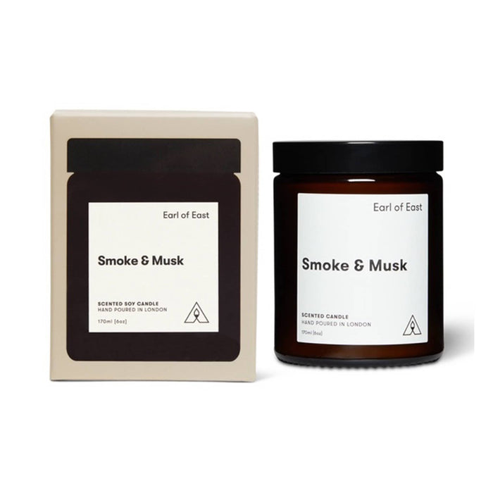 Earl of East Smoke & Musk scented soy candle shown with its cream-colored outer box and amber glass jar with a black lid on a white background.