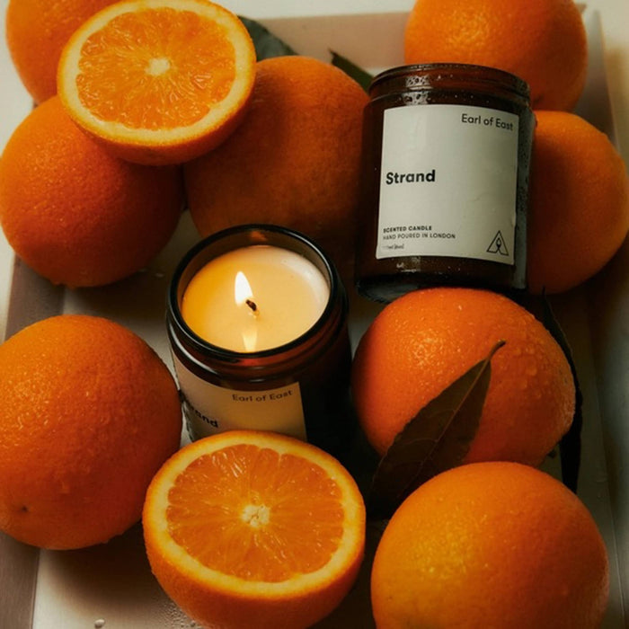 Candle with 'Strand' label surrounded by oranges.