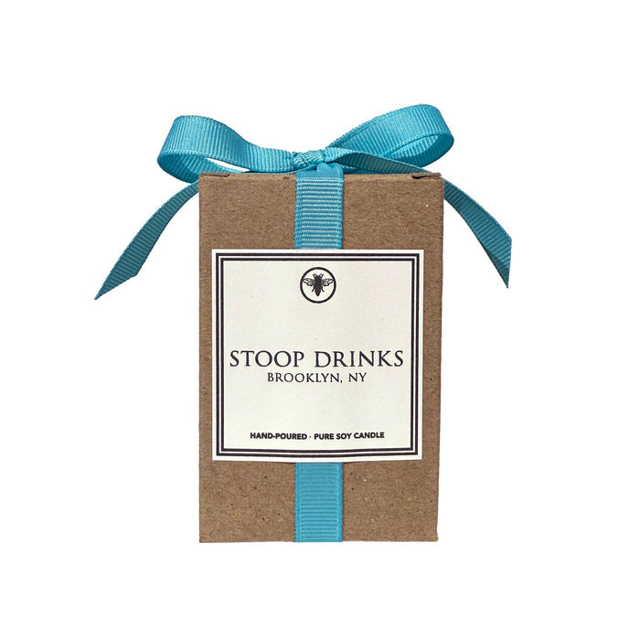 Ella B Candles "Stoop Drinks" scented candle in kraft box with a turquoise grosgrain ribbon on a white background.
