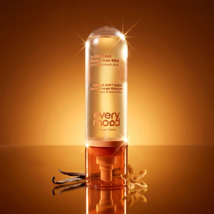 Bottle of Everymood Vanilla Soft Serve scented hydrating body and hair mist in clear and orange bottle on a reflective surface with an orange background.