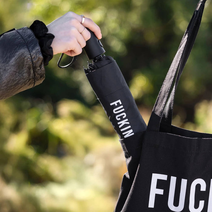 Person putting a black umbrella with a sleeve on it into a black bag in an outdoor setting.