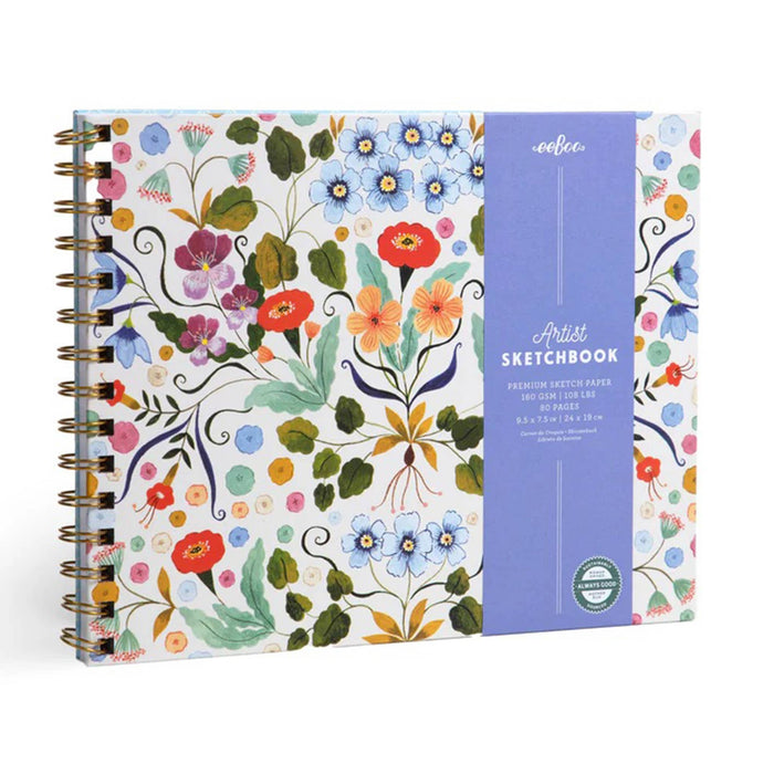 A spiral-bound artist sketchbook by eeboo, featuring a white cover decorated with a colorful watercolor floral pattern and a vertical lavender-blue paper band wrapped around the right side.