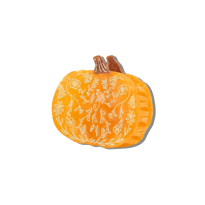 An orange pumpkin-shaped hair claw clip etched botanical design, front and side view with a soft gray shadow, centered on a plain white background.