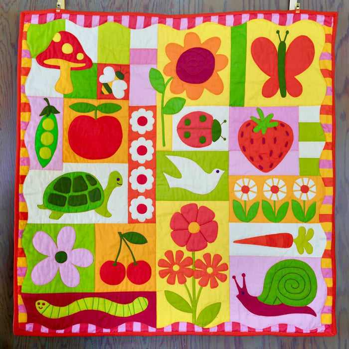 Children's quilt with colorful patterns of animals, fruits, and vegetables on a wooden surface.