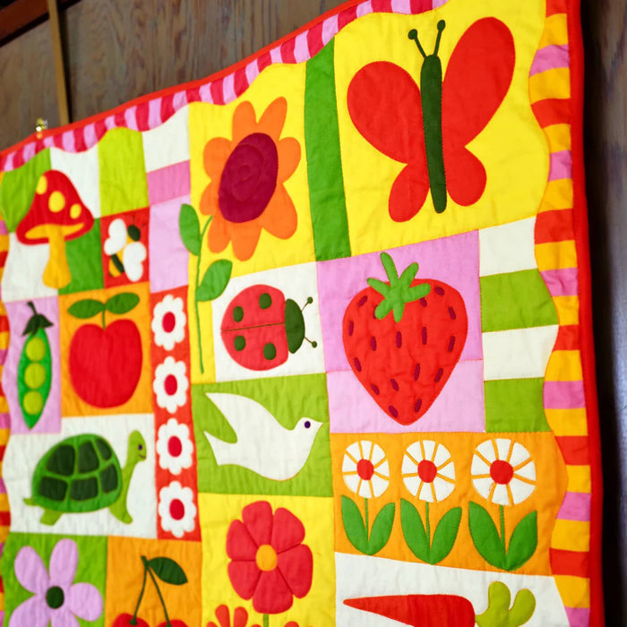 Detail of a colorful quilt with various patterns and shapes on a wooden surface.