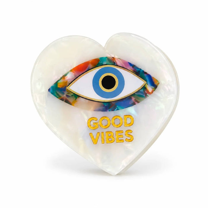 A heart-shaped acetate claw clip with a glossy white iridescent finish, featuring a colorful marbled evil eye design and the words 'GOOD VIBES' in gold lettering, set against a plain white background.
