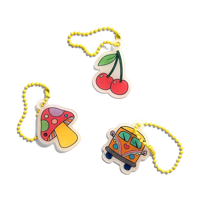 Three colorful acrylic keychains with yellow beaded chains, featuring a cherry, a mushroom, and a retro bus design on a white background.