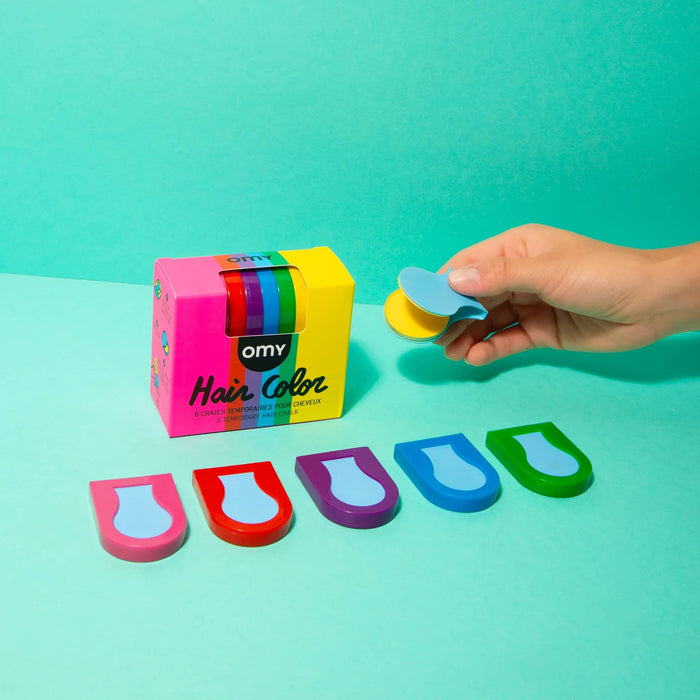 Pack of OMY temporary hair chalks in colorful packaging with sample chalks in front, on a green background.