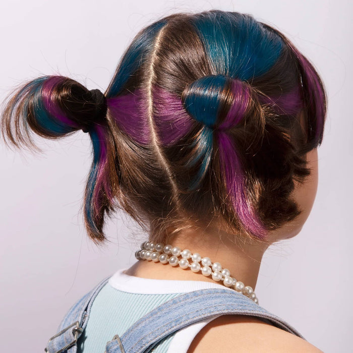 Person with colorful hair styled in pigtails wearing a pearl necklace on a light background.