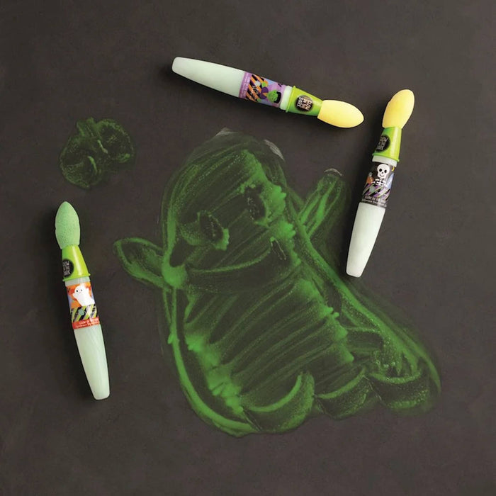 Three sponge paint brushes with Halloween illustrations on a black background, alongside a green painted ghost-like shape and a small green paint smudge.