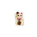 A small decorative maneki-neko charm shaped like a waving lucky cat, shown on a plain white background. The cat is cream-colored with red and black ears, a red collar, gold flower accents, and a brown bell with black Japanese characters.