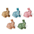 Five resin sitting rabbit figurines in different colors on a white background.