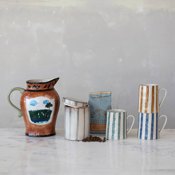 Collection of ceramic striped mugs, coffee holder and pitcher on a marble surface with a gray background.