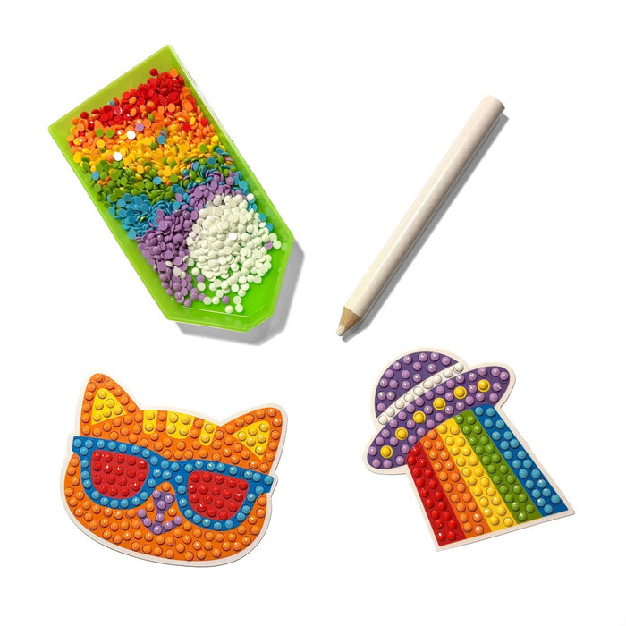 A green tray filled with colorful gem dots, white wax pencil and a cat face and UFO stickers with gems on them, shown on a plain white background.