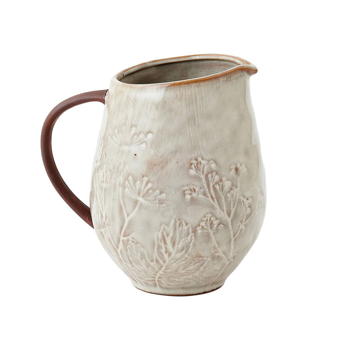 A handmade stoneware pitcher with a textured, off-white glaze featuring embossed botanical leaf patterns, a dark brown handle, and a brown rim, shown on a plain white background.