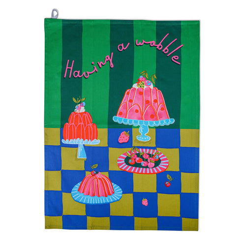 Tea towel with gelatin desserts on dessert plates on a blue and ochre surface with a two-tone green backdrop, flat on a white background.