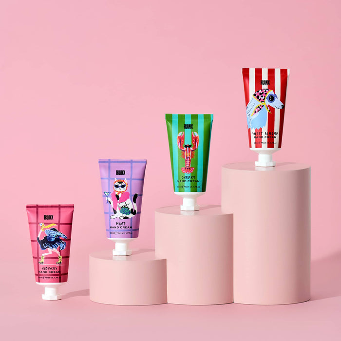 Four scented hand cream tubes displayed on pink cylindrical pedestals against a solid pink background. The tubes feature colorful, whimsical illustrations including an ostrich, lobster, cat, and dog.