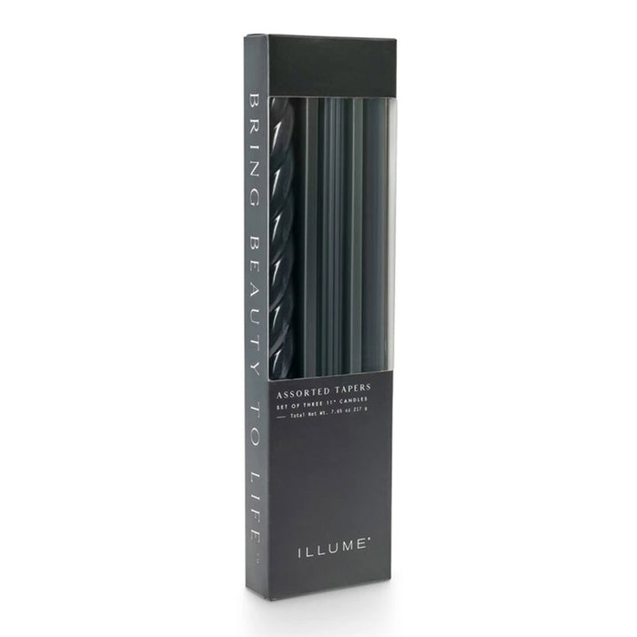 A tall rectangular box of ILLUME assorted taper candles in black, shown on a clean white background. The box has a clear window revealing the tapers inside.