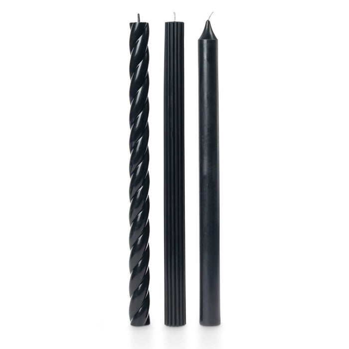 A set of 3 tall black taper candles in different textures, a twisted spiral, a ribbed and a smooth, standing upright on a white background.