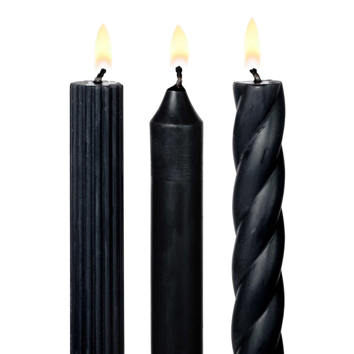 A set of 3 tall black taper candles in different textures, a twisted spiral, a ribbed and a smooth, standing upright on a white background, detail of lit wicks.