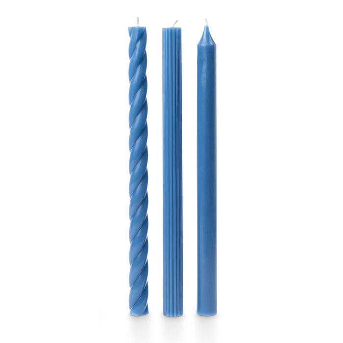A set of 3 tall blue taper candles in different textures, a twisted spiral, a ribbed and a smooth, standing upright on a white background.