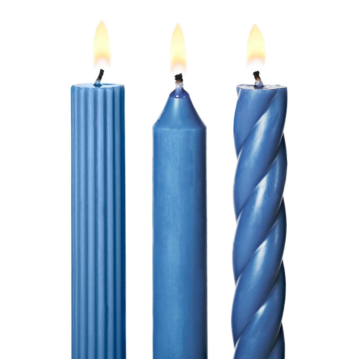 A set of 3 tall blue taper candles in different textures, a twisted spiral, a ribbed and a smooth, standing upright on a white background, detail of lit wicks.