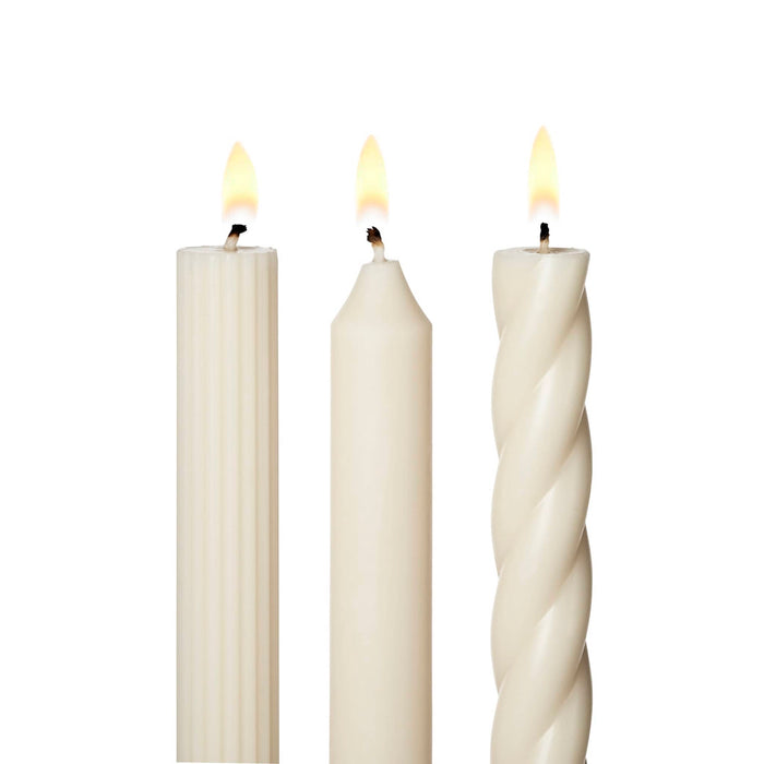 A set of 3 tall cream taper candles in different textures, a twisted spiral, a ribbed and a smooth, standing upright on a white background, detail of lit wicks.