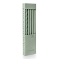 A tall rectangular box of ILLUME assorted taper candles in a sage green color, shown on a clean white background. The box has a clear window revealing the tapers inside.