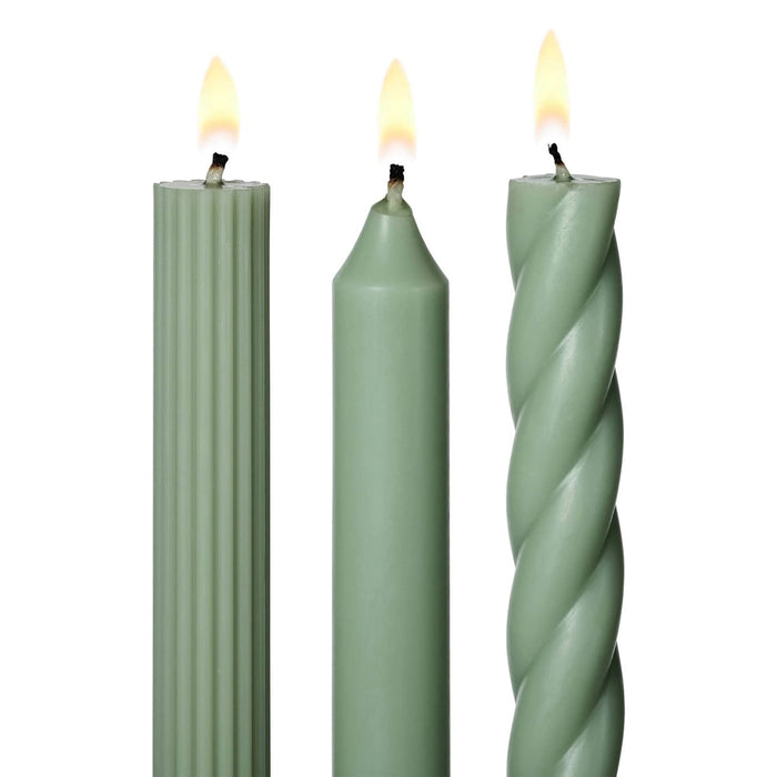 A set of 3 tall sage green taper candles in different textures, a twisted spiral, a ribbed and a smooth, standing upright on a white background, detail of lit wicks.