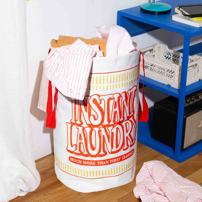 Laundry bag labeled 'Instant Laundry' filled with clothes next to a blue shelf.