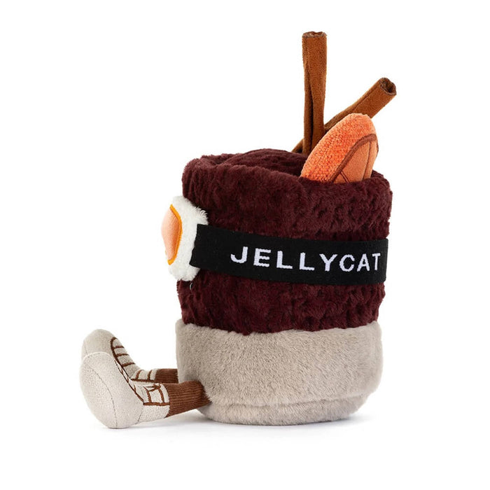 A plush toy shaped like a mulled spiced drink in a mug with a smiling face, wearing orange ski goggles and brown boots, side view, on a solid white background.