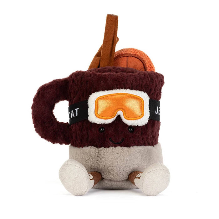 A plush toy shaped like a mulled spiced drink in a mug with a smiling face, wearing orange ski goggles and brown boots, front view, on a solid white background.