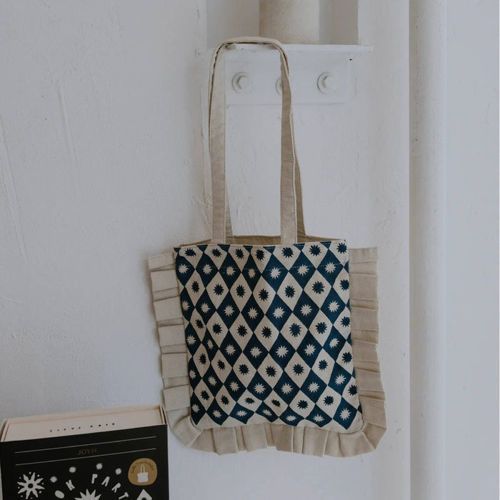 Ruffle tote bag with a blue block print pattern, hanging on a white wall.