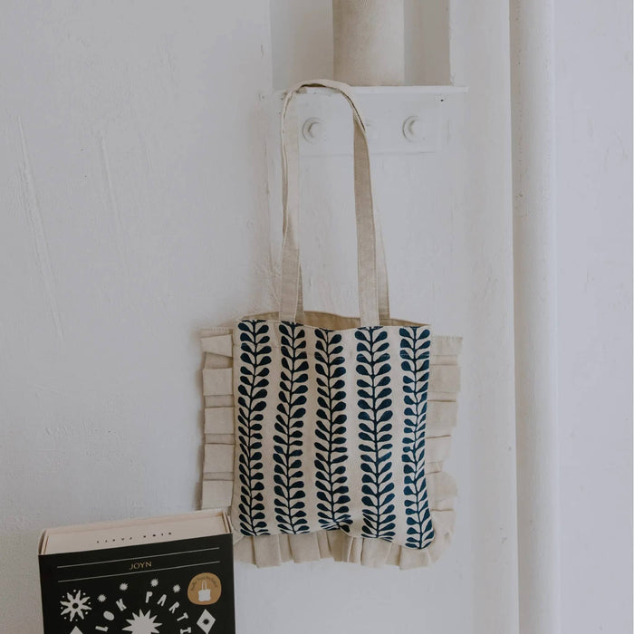 Ruffle tote bag with a blue leaf block print pattern, hanging on a white wall.