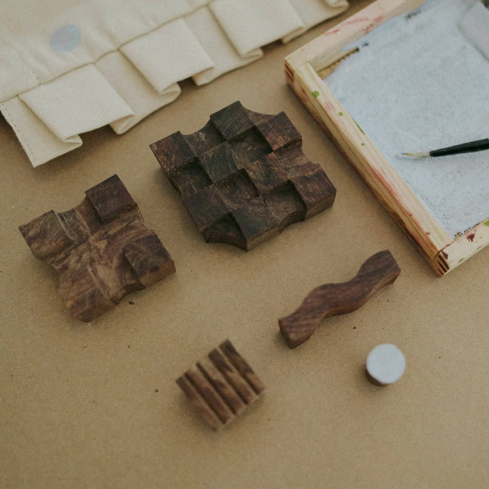 Wooden printing blocks on a textured surface with a paintbrush and canvas in the background.