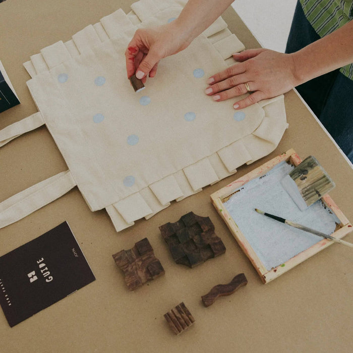 Person adding light blue dots using a wood print block, on a table.