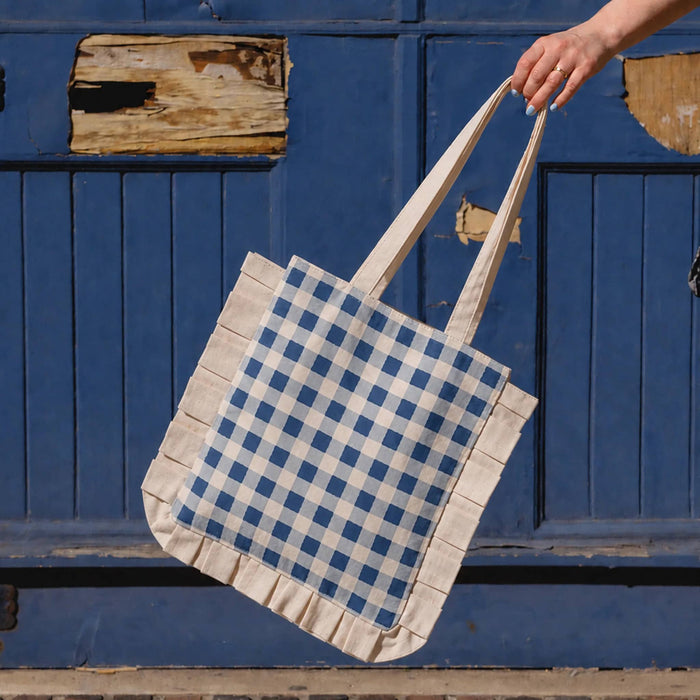 Tote bag with blue and white gingham pattern held by a hand against a blue wooden background.