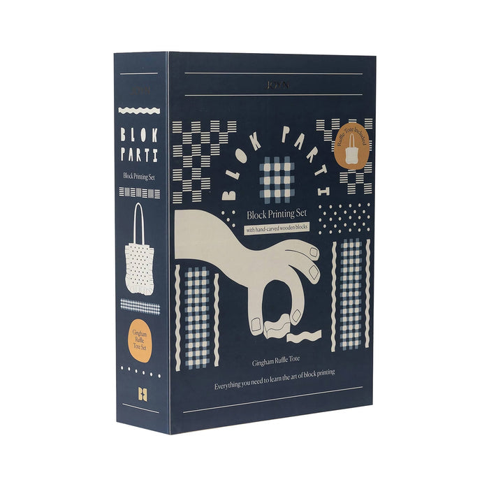Front angle view of the JOYN Blok Parti Gingham Ruffle Tote Block Printing Set, featuring a dark blue background with cream-colored block printing illustrations of hands, dots, and square patterns, on a plain white background.