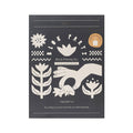 Front of JOYN Blok Parti Tulip Ruffle Tote Block Printing Set, featuring a dark charcoal gray background with cream-colored block printing illustrations of hands, tulip flowers and stem patterns, on a plain white background.
