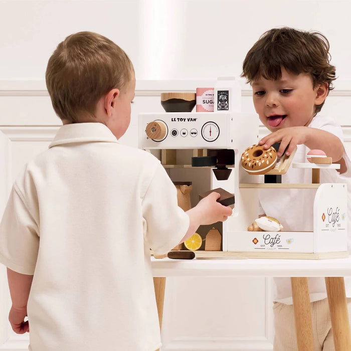 Two children playing with a toy coffee set on a white surface.