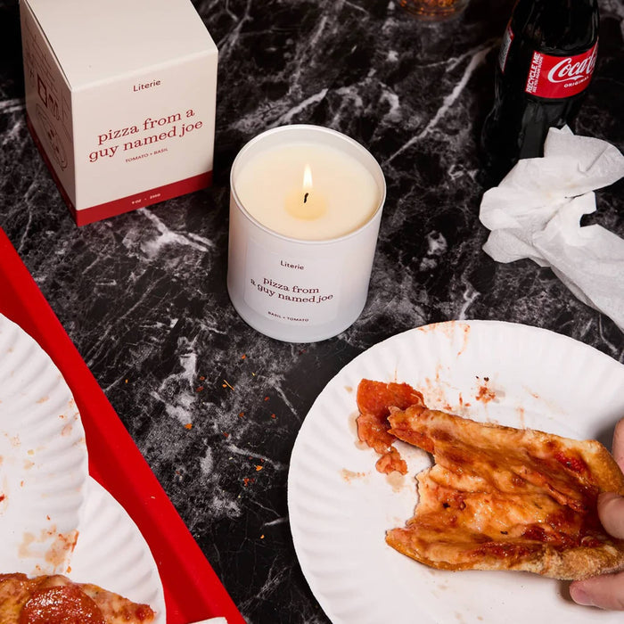 Candle labeled 'pizza from a guy named Joe' on a marble surface with pizza slices and a Coca-Cola bottle.