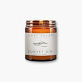 Lost Coast Sunset Dip white tea and ginger scented soy wax blend candle in amber jar, lid off and wick lit, on white background.