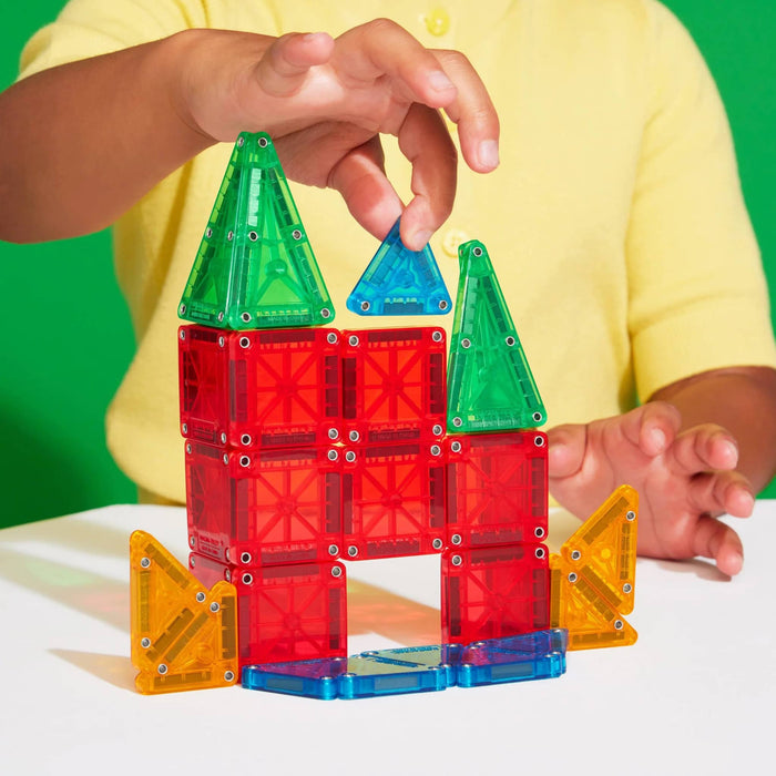 Child building a colorful castle with magnetic blocks on a white surface.