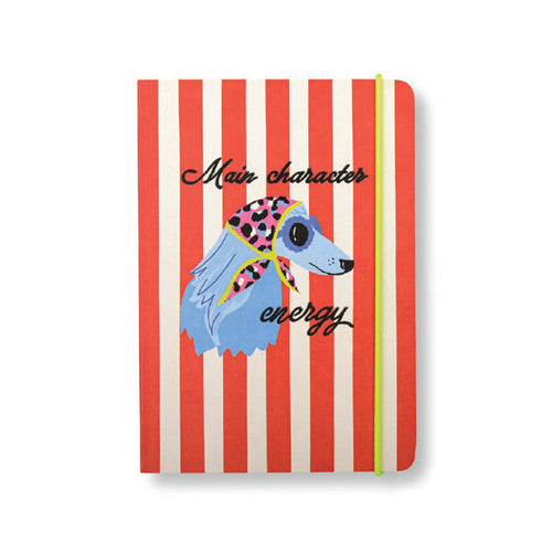 A softcover notebook with red and off-white vertical stripes, featuring a cartoon illustration of a blue dog wearing a pink polka-dot scarf on its head and sunglasses. The text 'Main character energy' is written in black script across the front, and a bright lime green elastic closure band is visible on the right side.